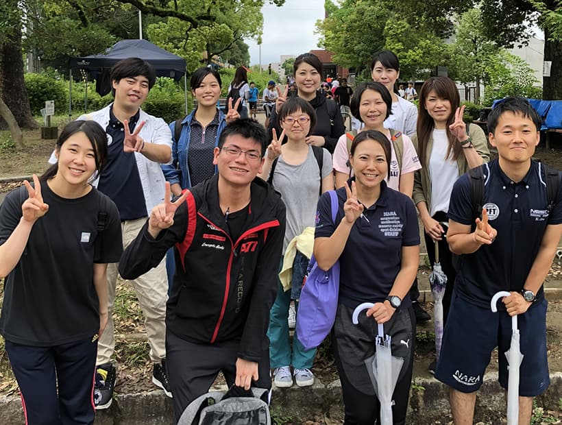 屋外で集合写真を撮る学生たち。皆が笑顔でピースサインをしている様子