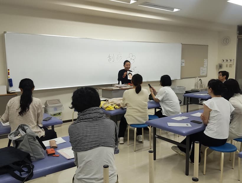 講師が教材を使いながら、机に座った学生たちに向けて授業を行う様子