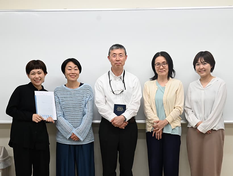 ホワイトボードの前で並んで立つ担当教員と学生たちの集合写真