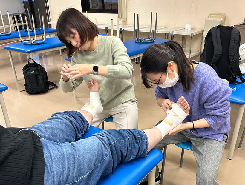 実習室で足首にテーピングを行う学生たちの様子