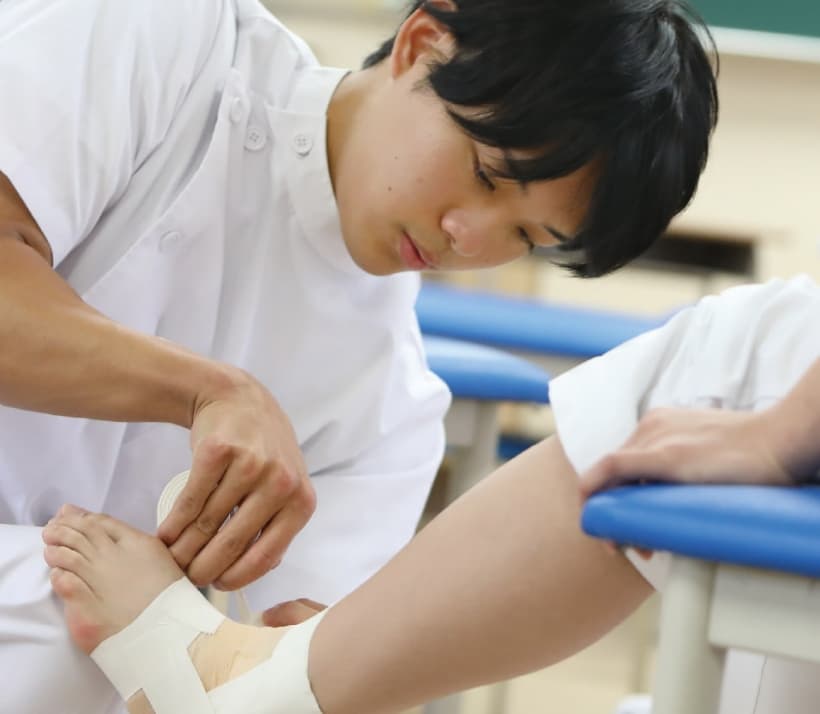 柔道整復師が患者の足首にテーピングを行う実習の様子