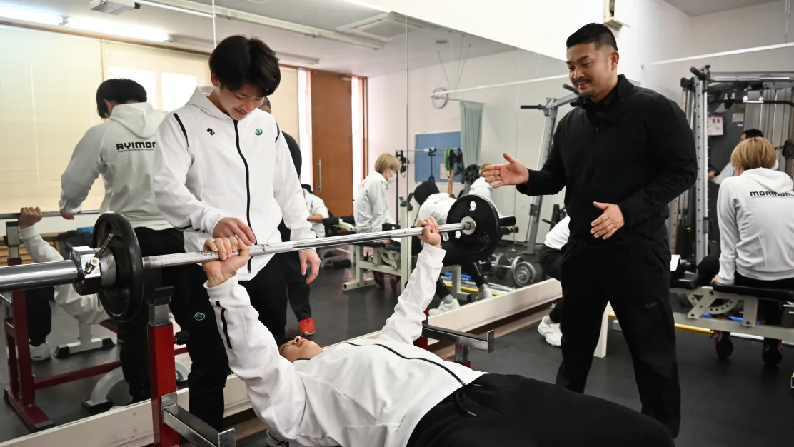 トレーナーの指導を受けながらトレーニングする学生